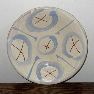 May include: A white ceramic bowl with a blue and red abstract design. The bowl has a circular shape and is decorated with blue circles and red X shapes.