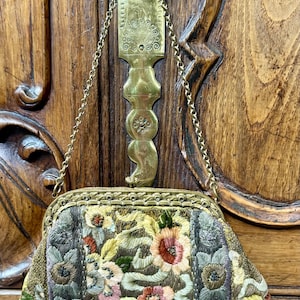 May include: An antique floral embroidered purse with a gold chain strap. The purse features a detailed pattern of pink, yellow, and green flowers on a dark background. The frame and chain are gold-toned, and the purse hangs from a decorative brass fixture.