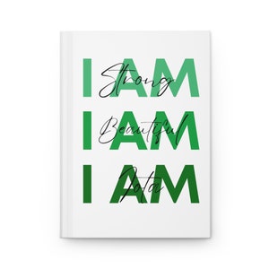 May include: A white journal with the words "I AM" repeated three times in green text. The words "strong", "beautiful", and "enough" are written in black cursive script above each "I AM".