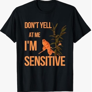 Könnte beinhalten: Schwarzes T-Shirt mit dem Text "DON'T YELL AT ME I'M SENSITIVE" in Orange. Das Shirt zeigt eine orangefarbene Illustration einer Eidechse oder eines Geckos mit grünen Pflanzenblättern.