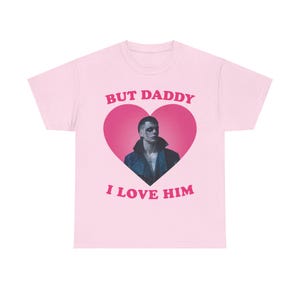 Puede incluir: Camiseta rosa con un gráfico de corazón rosa que presenta a un hombre con un ojo negro y el texto "But Daddy I Love Him".