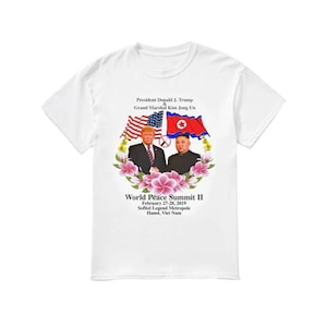 May include: White t-shirt featuring a graphic of Donald J. Trump and Kim Jong Un, with the American and North Korean flags. The text reads "World Peace Summit II" and the location and date of the summit.