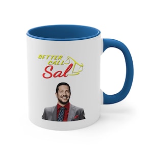 May include: White ceramic coffee mug with a blue rim and handle. The mug features a graphic of a man with a beard and a yellow and red logo that says "Better Call Sal" with a scale design.