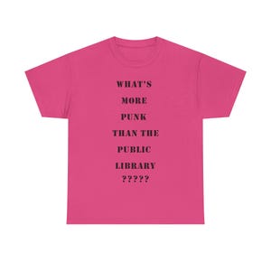 以下が含まれることがあります： ピンクのTシャツに、黒い文字で「What's More Punk Than The Public Library?????」と書かれています