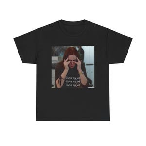 May include: Black t-shirt featuring a meme of a woman with her hands on her face. The image has the text "i love my job" repeated three times in a white, sans-serif font. The t-shirt is a crew neck and appears to be made of cotton.