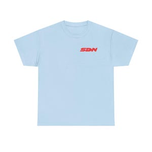 May include: A pale blue t-shirt with a crew neck. The shirt has the red letters "SDN" printed on the upper left chest. The t-shirt is made of a soft material.