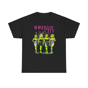 Pode incluir: Camiseta preta com uma estampa gráfica de Shrek e três personagens femininas em frente a um horizonte urbano. O texto "Shreks and the City" é impresso em rosa acima dos personagens.