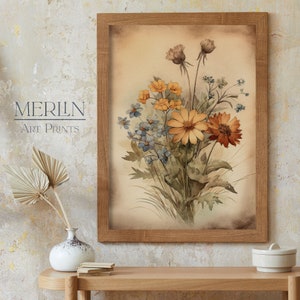 K&ouml;nnte beinhalten: Ein gerahmtes Aquarellbild eines Strau&szlig;es gelber, orangefarbener und blauer Wildblumen. Die Blumen sind in einer Vase arrangiert und vor einem hellbraunen Hintergrund platziert.