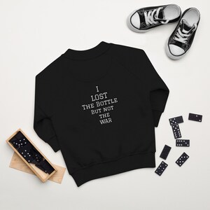 May include: Black sweatshirt with a white embroidered quote: "I lost the bottle but not the war".