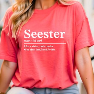 May include: Coral-colored t-shirt with the word "Seester" in white, along with a definition. The definition reads "Like a sister, only cooler. See also: best friend for life."