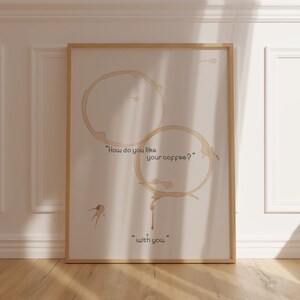 K&ouml;nnte beinhalten: Ein wei&szlig;er gerahmter Poster mit zwei Kaffeeflecken und dem Text "Wie m&ouml;gen Sie Ihren Kaffee? ... mit Ihnen."