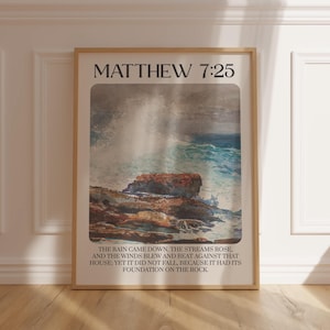 Puede incluir: Una impresión enmarcada con una pintura de acuarela de una costa rocosa con olas rompiendo. La impresión tiene el texto "Mateo 7:25" en la parte superior y un versículo bíblico sobre la construcción de una base sobre la roca.