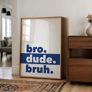 May include: A framed poster with the words "bro. dude. bruh." in bold, white letters on a blue background. The poster is hanging on a white wall in a hallway.