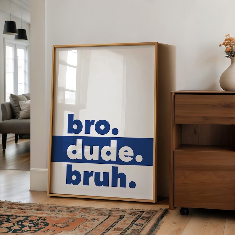 May include: A framed poster with the words "bro. dude. bruh." in bold, white letters on a blue background. The poster is hanging on a white wall in a hallway.