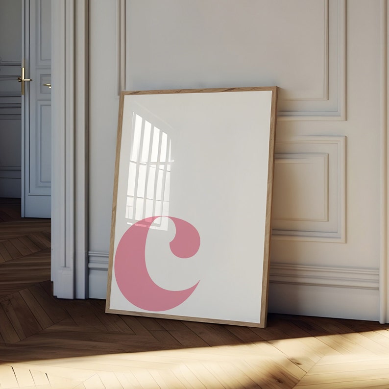 Pu&ograve; includere: Una stampa incorniciata con una lettera "C" rosa su sfondo bianco. La cornice &egrave; in legno e ha una finitura naturale.