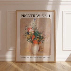Può includere: Una stampa incorniciata con una citazione da Proverbi 3:3-4, "Che l'amore e la fedeltà non ti lascino mai..." La stampa presenta un dipinto di un mazzo di fiori colorati in un vaso bianco su uno sfondo rosa chiaro.
