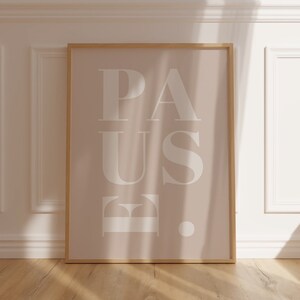 May include: A framed print with a light brown background and white text that reads "PAUSE" with a period after the E. The print is in a light wood frame.