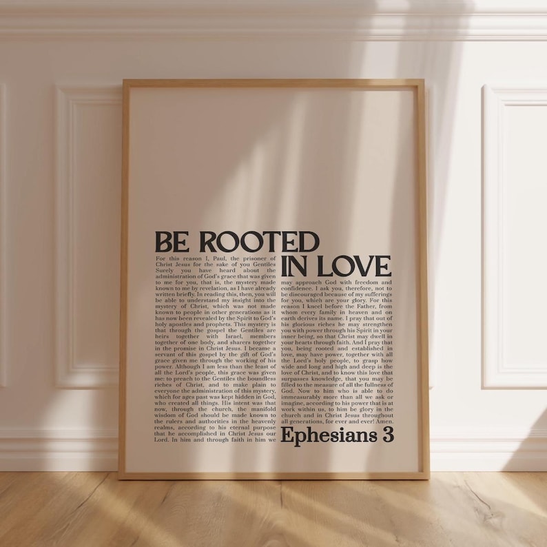 May include: A framed print with the words "BE ROOTED IN LOVE" in bold, black text. The print also includes a passage from Ephesians 3. The frame is a light wood color.