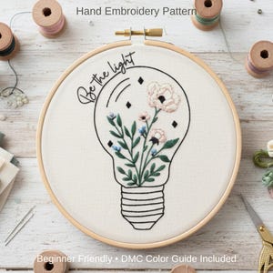 May include: Embroidery hoop featuring a lightbulb design filled with embroidered flowers and greenery. The words "Be the light" are written in cursive. The text "Beginner Friendly • DMC Color Guide Included" is also visible.