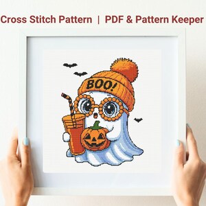 May include: Cross stitch pattern featuring a cute ghost wearing an orange beanie with the word "BOO!" and glasses, holding a pumpkin and a drink. The ghost is white with blue shading. Includes PDF & Pattern Keeper.