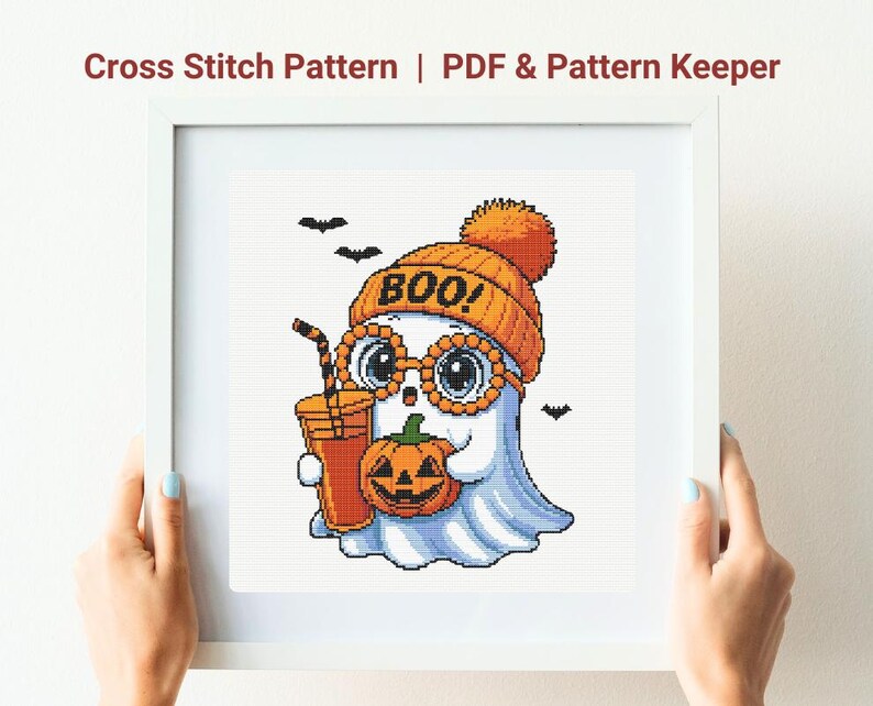 May include: Cross stitch pattern featuring a cute ghost wearing an orange beanie with the word "BOO!" and glasses, holding a pumpkin and a drink. The ghost is white with blue shading. Includes PDF & Pattern Keeper.