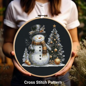 May include: A cross-stitch pattern featuring a snowman wearing a top hat and scarf, standing next to a decorated Christmas tree. The design includes gold ornaments and a small gift. The text "Cross Stitch Pattern" is at the bottom.