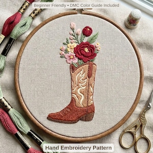 May include: Hand embroidery pattern featuring a brown cowboy boot filled with red, pink, and yellow flowers. The embroidery is set in a wooden hoop with the text "Beginner Friendly • DMC Color Guide Included" and "Hand Embroidery Pattern".