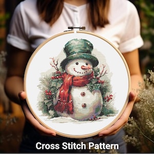 May include: A cross stitch pattern featuring a snowman with a green hat and red scarf, surrounded by holly and berries.