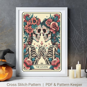 May include: Cross stitch pattern of a tarot card depicting two skeletons with floral crowns, holding hands and looking at each other. The card is titled "The Lovers".