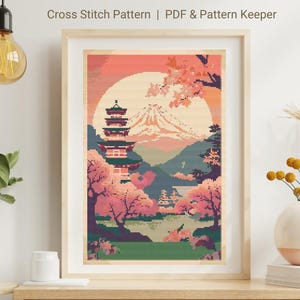 Può includere: Schema di punto croce di un paesaggio giapponese con una pagoda, fiori di ciliegio e il monte Fuji sullo sfondo. Lo schema è in una cornice e ha una combinazione di colori rosa, arancio e verde.