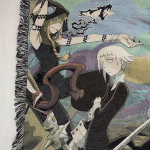 Op de afbeelding: Een wandkleed met twee anime-personages, een met lang blond haar en een zwarte kapmantel, de ander met wit haar en een zwarte jas. Het wandkleed heeft een blauwe en paarse achtergrond met een draaiend patroon.