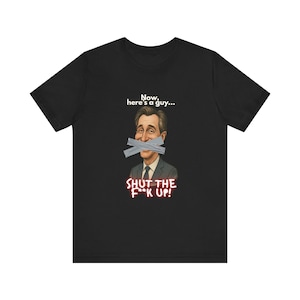 May include: Black t-shirt with a graphic of a man's face with tape over his mouth. The text above the image reads "Now, here's a guy..." and the text below reads "SHUT THE F*CK UP!"