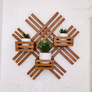 May include: A wooden wall-mounted planter with a geometric design. The planter features four small, square wooden boxes, each holding a small green plant in a white ceramic pot. The wooden structure is made of thin, brown wooden slats.