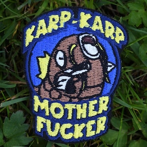 May include: Embroidered patch with a cartoon character in brown, white, and black, set against a blue background. The patch features the text "KARP-KARP" and "MOTHER FUCKER" in yellow, with a blue border.