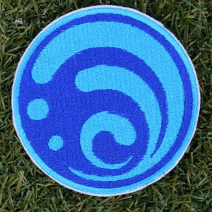May include: A blue and white embroidered patch with a stylized wave design. The wave is blue with a white outline and is set against a white background.