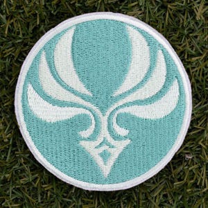 May include: A white embroidered design of a stylized bird with wings spread on a light blue circular patch.