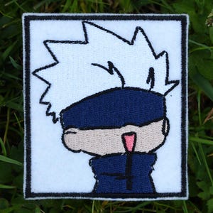 Può includere: Toppa ricamata bianca e blu di un personaggio dei cartoni animati con capelli bianchi a punta, una maschera per gli occhi blu e una camicia blu. Il personaggio sorride con la lingua fuori.