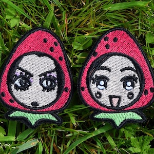 Könnte beinhalten: Zwei gestickte Aufnäher in Form von Erdbeeren mit Gesichtern. Die Erdbeeren sind rot mit schwarzen Samen und grünen Blättern. Die Gesichter haben große Augen und sind schwarz umrandet.