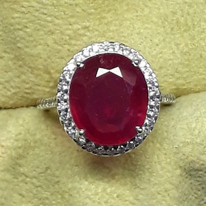 May include: A silver ring with a large oval ruby surrounded by a halo of smaller diamonds.
