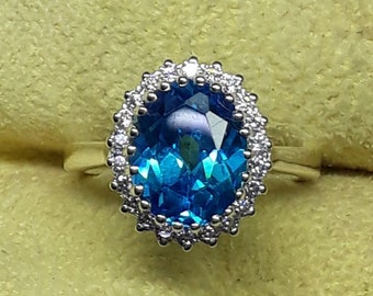 May include: A silver ring with a large oval blue topaz gemstone surrounded by a halo of smaller diamonds.