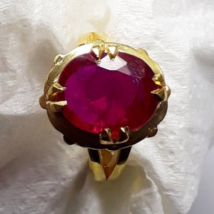 Op de afbeelding: Een gouden ring met een grote, ovale, felroze edelsteen die in een klauwzitting is gezet. De ring heeft een eenvoudige band.