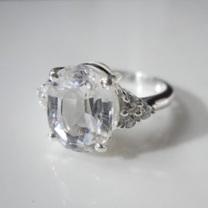 May include: A silver ring featuring a large, clear, faceted gemstone and smaller clear gemstones on the band.