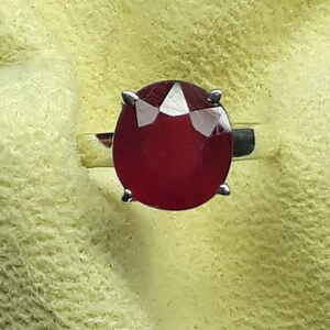 May include: A silver ring with a large, deep red gemstone set in a prong setting.