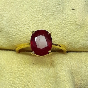 May include: A gold ring set with a large, oval ruby gemstone.