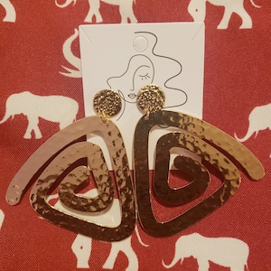 May include: A pair of gold-toned earrings with a hammered texture. The earrings are shaped like a triangle with a spiral design.