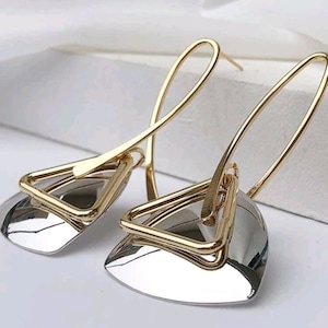 May include: A pair of gold and silver earrings with a geometric design. The earrings feature a triangle shape with a smaller triangle inside. The earrings are long and dangle.