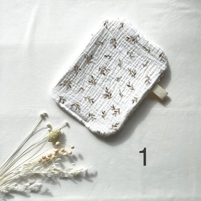 May include: White, rectangular baby washcloth with a brown leaf pattern. The washcloth has a loop on one side and is made of a textured fabric. The number "1" is printed in black on the white background.
