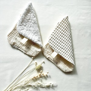 May include: Two white and cream-colored baby washcloths. One washcloth has a textured, fluffy surface, and the other has a waffle weave. Both have a cream-colored patterned backing and a small white tag.