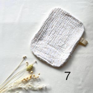 May include: A white and beige washcloth with a loop, made of a textured fabric. The washcloth is rectangular with rounded edges. The number 7 is printed in black on the bottom right corner of the image.