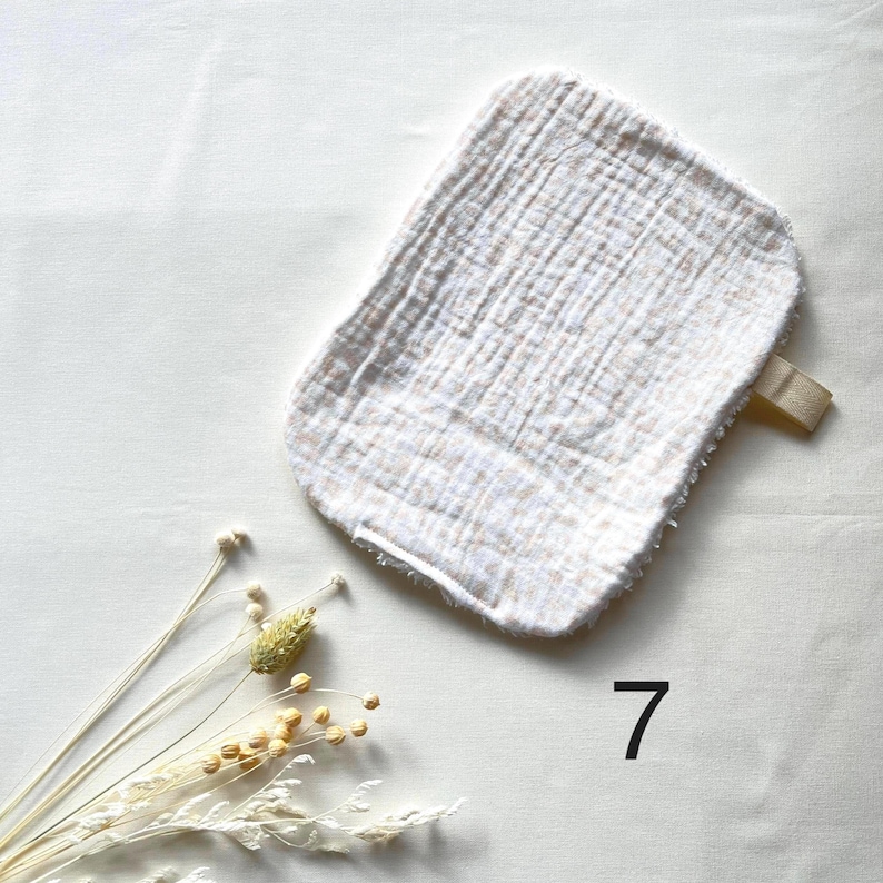 May include: A white and beige washcloth with a loop, made of a textured fabric. The washcloth is rectangular with rounded edges. The number 7 is printed in black on the bottom right corner of the image.
